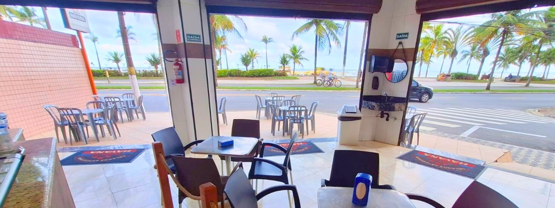 Vista interna mostrando as mesas e a praia ao fundo.